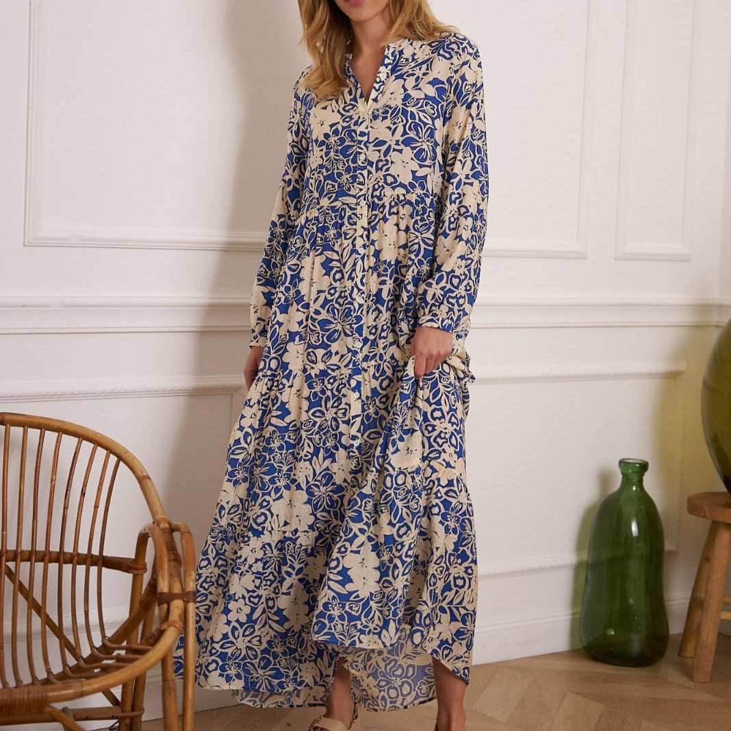 Beige-blaues Maxikleid mit langem Schnitt, Blumenmuster und langen Ärmeln, getragen von einer Frau in Sandalen