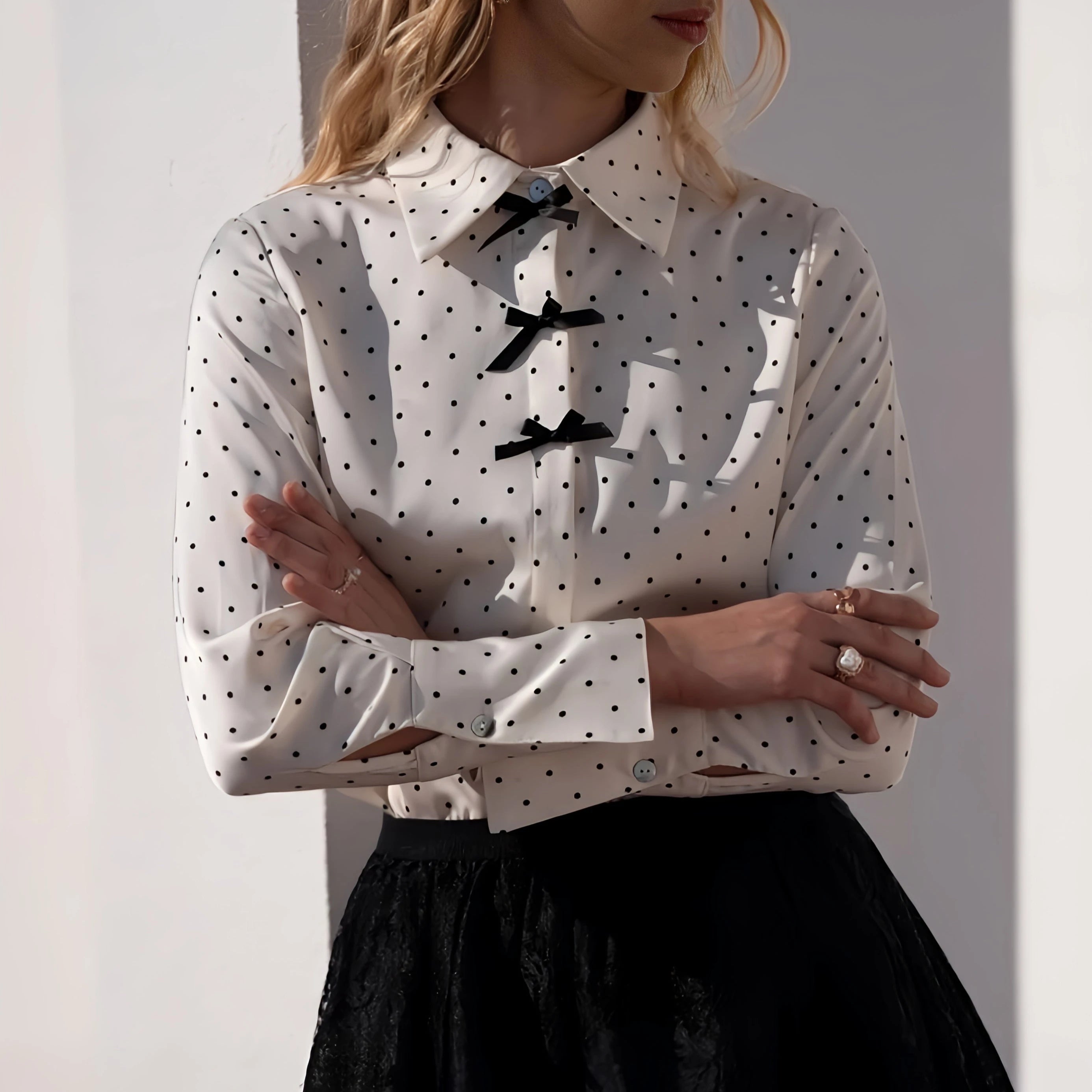 Weiße elegante Hemdbluse Charlotte mit schwarzen Polka-Dots und dekorativen Schleifen am Kragen, langen Ärmeln und figurbetontem Schnitt.