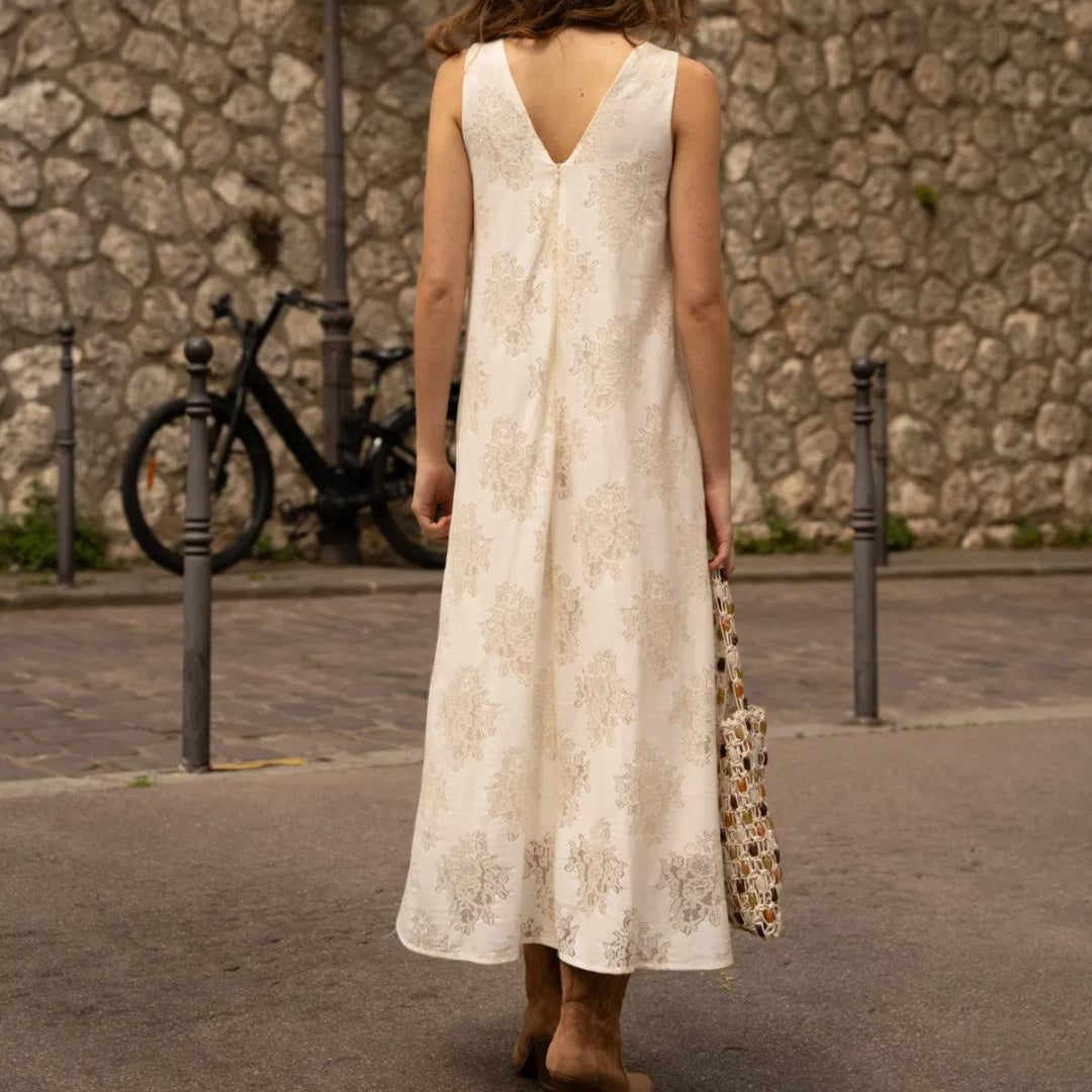 Maxi-Kleid Creme mit Blumen-Stickerei – Rückansicht mit tiefem V-Ausschnitt, getragen auf gepflasterter Straße